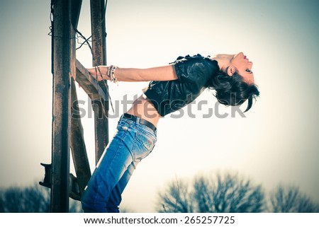 young rebel woman in blue jeans and leather jacket outdoor shot on old metal construction hot sunny day