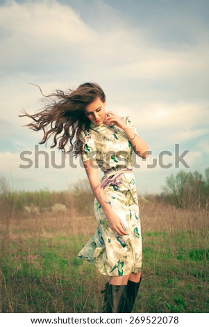 young woman in summer dress in grass field, hair in motion from wind, retro look and colors