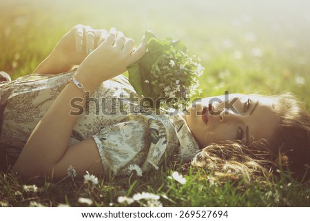 delicate beautiful young woman enjoy in sun lie in grass hold bouquet of wild flowers retro look and colors
