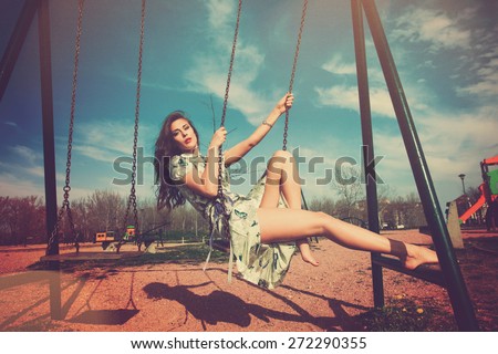 barefoot young woman sit on swing in summer dress in playing park , full body shot, retro colors, color leek texture added