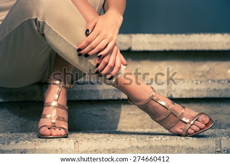 woman legs in high heel golden sandals and pants sit on stairs, outdoor shot, close up