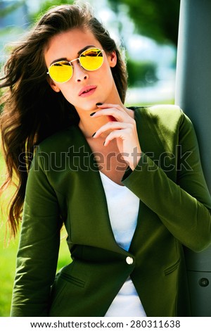 young urban fashion woman wearing yellow sunglasses and green jacket, outdoor shot in the city
