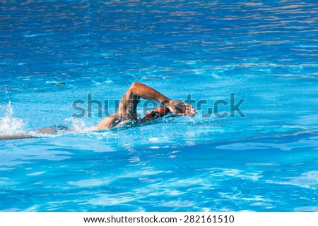 young man swim crawl style in outdoor swimming pool, sunny summer day