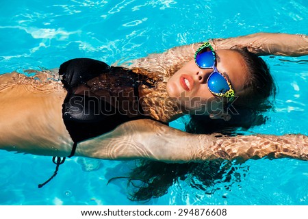 young attractive woman in black bikini and sunglasses in pool, from above