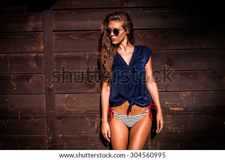 beautiful tanned young woman in bikini and navy blue summer shirt against wooden wall outdoor shot hot summer day