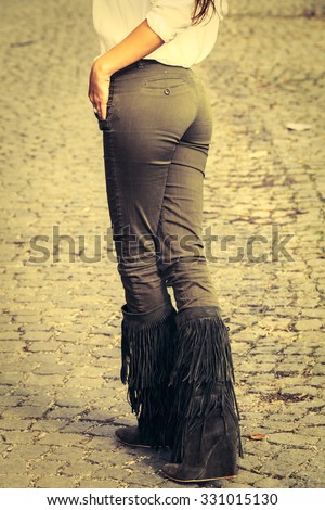 woman legs in green tight pants and tassel boots, stand on cobble, retro colors