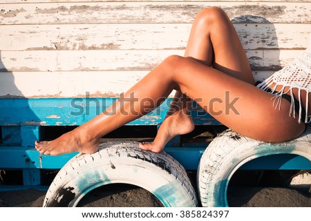 tanned woman legs on tires by wooden house at sea sunny summer day, side view