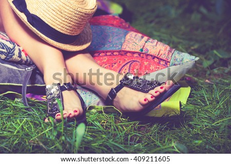 woman feet on grass in flat summer sandals lean on pillows  hat lay on legs