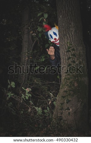 scary clown behind tree inviting with hand gesture night scene