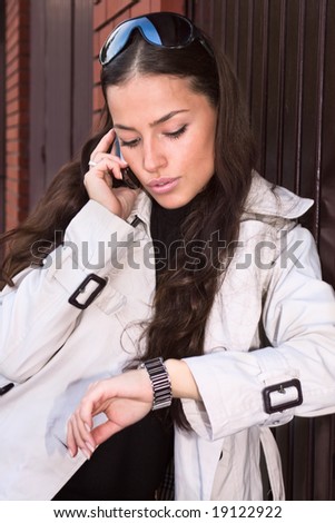 woman talking on cellphone and looking at watch, outside shot