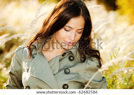 young woman in topcoat walking accros the autumn meadow, sunny autumn day