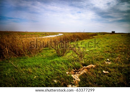 sheep-walk near the small river with green grassa and bushes and  shepherd\'s huts in the distance