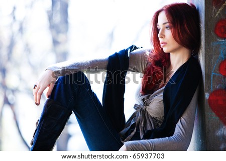 young red hair woman in casual clothes sit on banch, outdoor shot