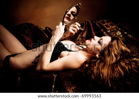 woman hold hand mirror and apply lipstick, lie on bed, golden brown background, studio shot
