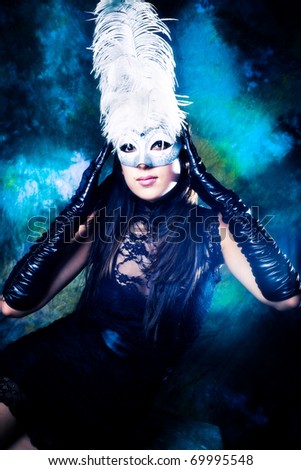 young woman wearing white venetian mask with feathers, black dress and long black gloves, studio shot