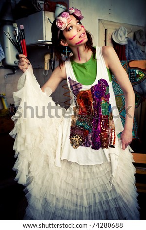 woman in artist studio with paint on face  holding paint brushes in hand looking for inspiration