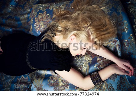 blond woman in black dress lie  on baroque floral fabric, studio shot