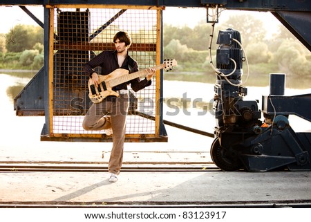 young handsome man play guitar, outdoor shot by the river in harbor