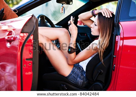 young woman sitting in red sport car with mobile phone