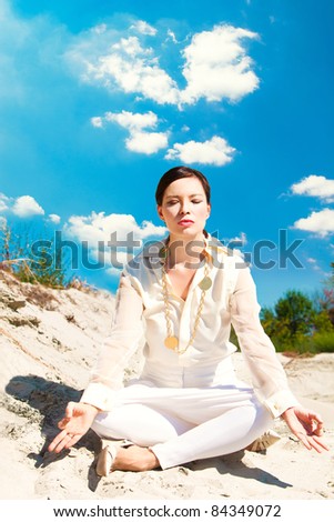 adult woman in elegant light summer clothes meditate on sand, outdoor shot, summer day