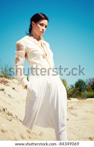 beautiful woman in elegant summer clothes , sand and blue sky, summer day, small amount of grain added