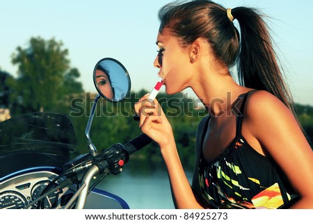 young woman applying lipstick against mirror on bike, outdoor shot at sunset