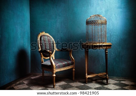 Louis table, armchair and old golden bird cage in blue room with tiled floor