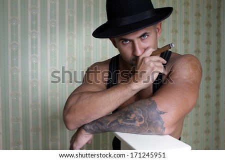 macho man with athletic body in felt hat with a cigar in his hand and a smile on his face