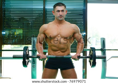 The young sports athlete is engaged in a gym with dumbbells and showing the sound body