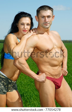two youths of sportsman a girl and fellow sit showing the sporting bodies on a background sky and grass