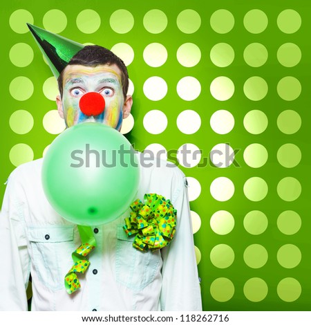 Excited Male Clown With Colourful Face Paint Blowing Up A Green Balloon While Having Fun Celebrating Kids Birthday Parties