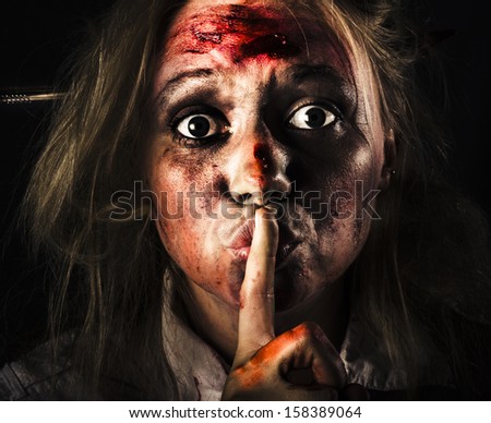 Close-up halloween portrait of a scary zombie horror face gesturing silence at the dead of night with bloody terror