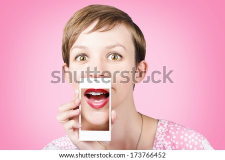 Studio portrait of a happy young girl pulling a surprised funny face while on a video call to girlfriends through a cellphone, over pink background