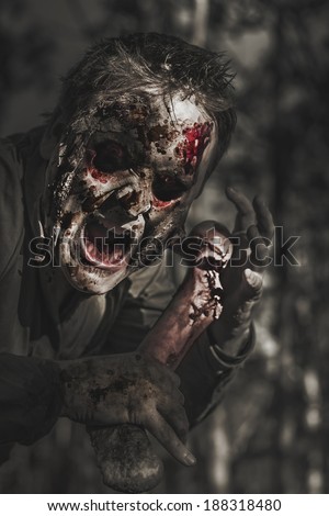 Spooky horror photograph of an evil male zombie with rotten face shouting out in bloody terror at dark haunted forest. The bone collector