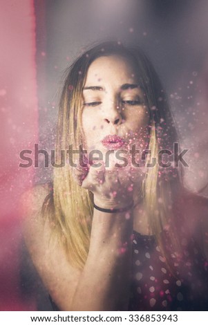 Creative pink abstract portrait on the face of a beautiful woman blowing a burst of magic glitter at valentine\'s day party celebration. Valentine girl making wish kiss