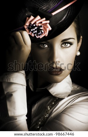 Close-up portrait on the face of a beautiful and mysterious female standing in the shadows halfway between dark and light wearing a stylish flower hat in a image titled face of dark fashion