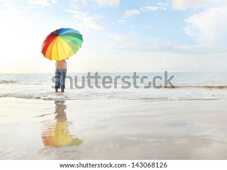 Girl walking along the beach with colour full umbella.