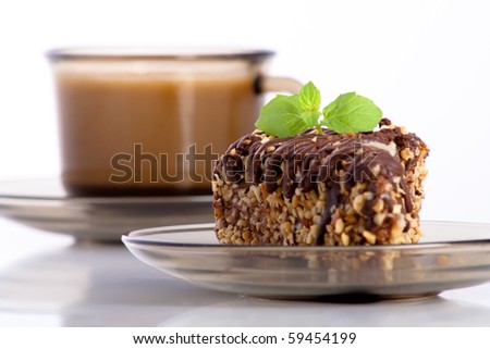 chocolate cake with nuts decorated with mint and a cup of coffee in background