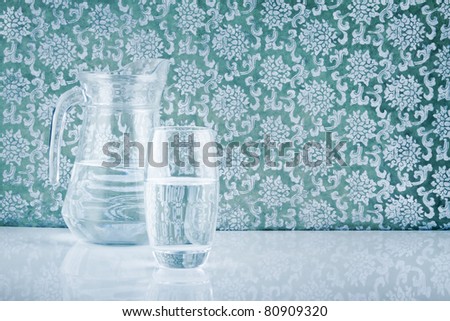 glass and jug filled with fresh water on patterned backdrop