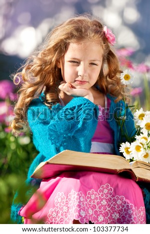 Girl reading a thick book in a flowering garden. child with a bouquet of daisies and a book sitting in the garden