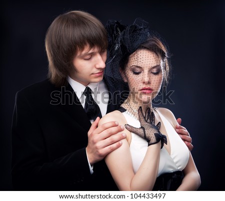 the man in a suit gently embraces the girl in a dress. studio shooting at black background