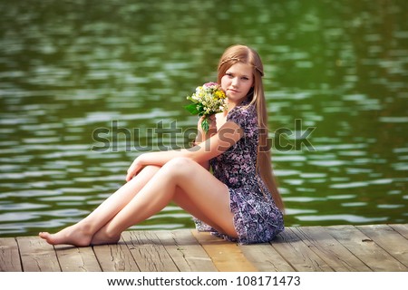 Girl sits on a wooden pier. she holds a bunch of flowers. Outdoor photo on the background of water.