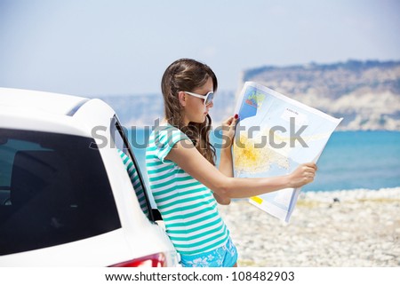 Travel - young woman with car look at road map on a beach against sea and sky