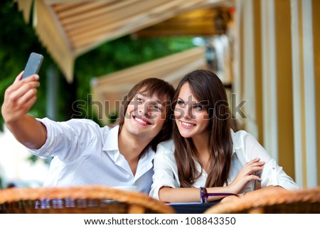 couple on a date in summer cafe - happy guy and a girl doing a photo on the cell phone