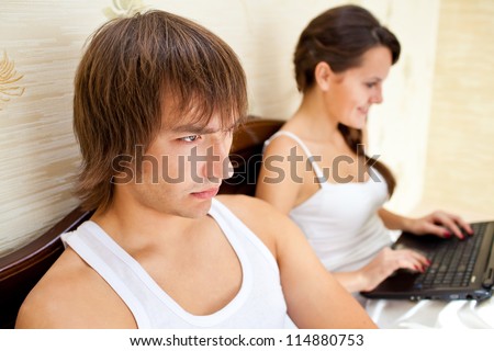 Couple with laptop in a bed. Man is angry, woman is busy and works on computer. relationship problems concept