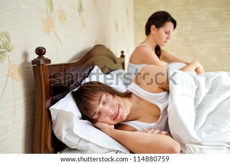 married couple in a bedroom. The girl is upset, and the guy sleeps happy