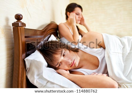 couple in a bedroom. the guy is upset, the girl with headache holds the head