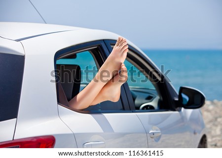 Concept of summer car trip vacation . Woman legs out the window in car at background of sea water. Conceptual travel ,freedom and holidays image.