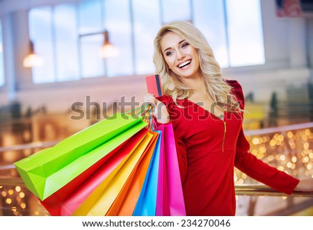beautiful young woman holding colored shopping bags and credit card in the shopping mall on sales