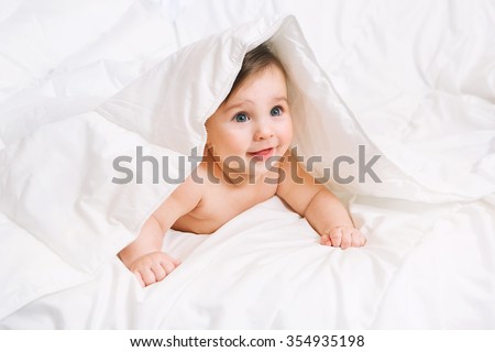 Surprised Baby lies on the bed under the blanket